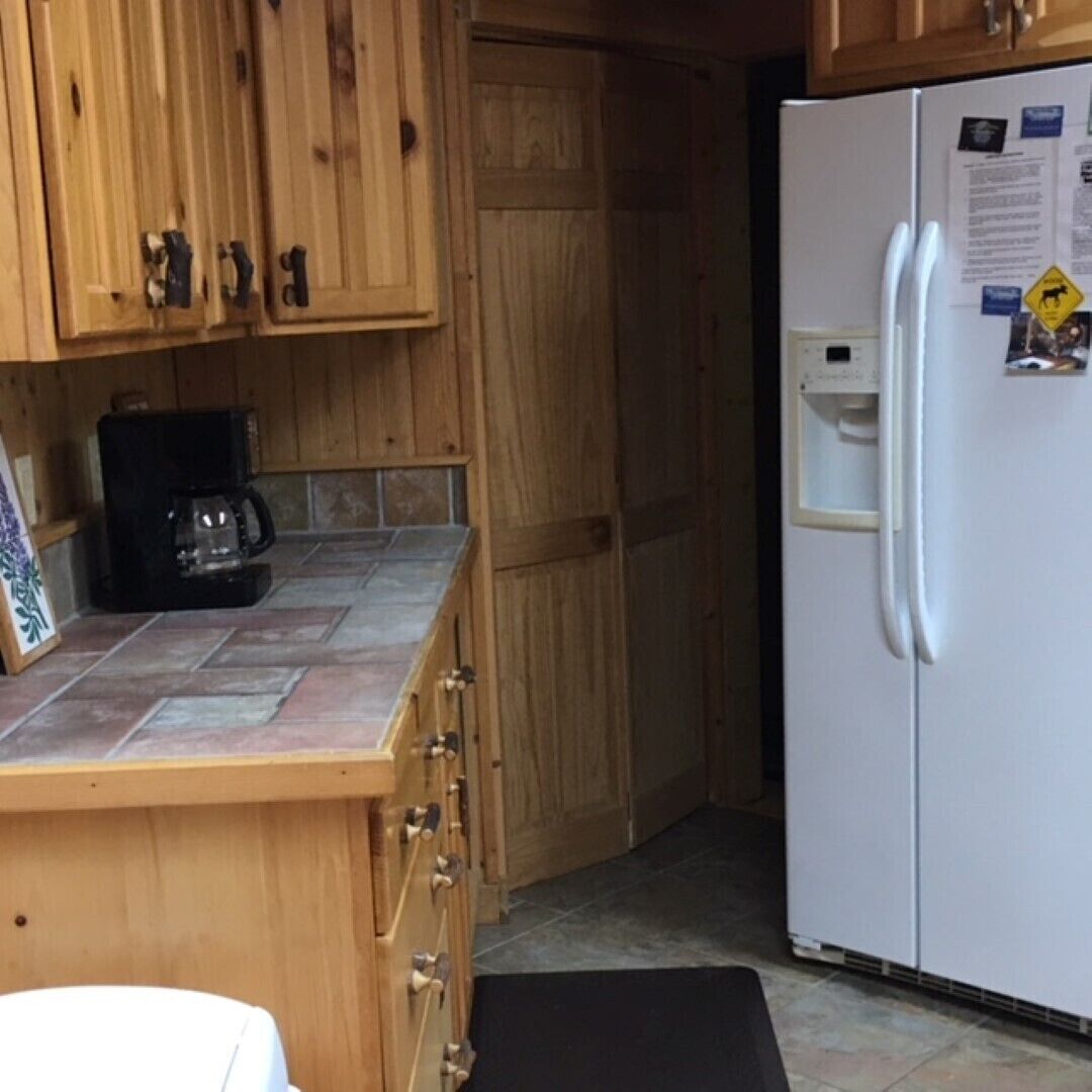 A kitchen with wooden cabinets, a coffee maker, and a white refrigerator with magnets and papers.