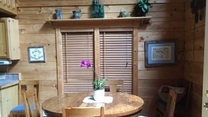 Interior de madeira com uma mesa de jantar redonda, cadeiras com almofadas azuis e uma planta em vaso sobre a mesa.