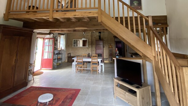 En rummelig loftetage med en trætrappe, et spiseområde og et fjernsyn i stuen.
