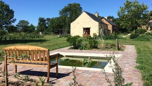 En træbænk, et lille bassin og et hus med en røddoor.