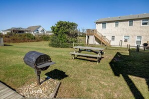 Ein Garten mit Grill, Picknicktisch und einer Holzterrasse.