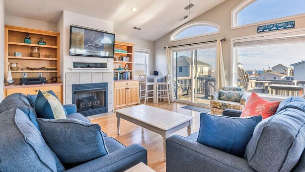 A spacious living room with a fireplace, comfortable seating, a television, and a large window offering a view of the surrounding area.