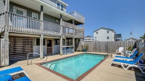 A two-story building with a swimming pool, a covered patio, and a fenced backyard.