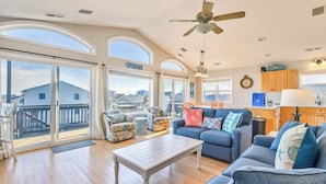 A spacious living room with a large sliding glass door leading to a balcony, a ceiling fan, and a view of houses in the distance.