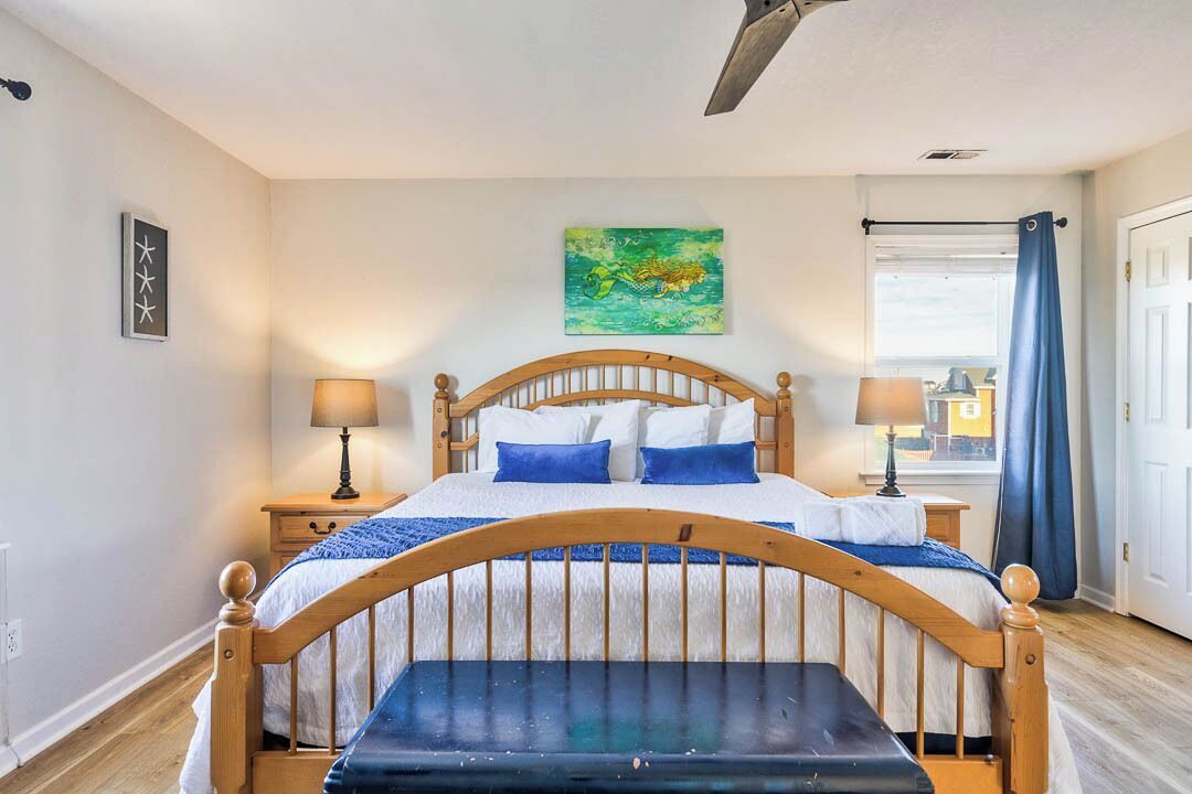 Een slaapkamer met een houten bed, twee nachtkastjes met lampen, een blauw gordijn en uitzicht op de stad.