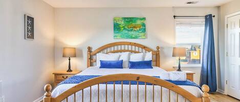 Een slaapkamer met een houten bed, twee nachtkastjes met lampen, een blauw gordijn en uitzicht op de stad.