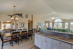 A spacious kitchen with a large island, dining area with chairs, and a view of the outdoors through large windows.