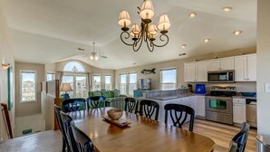 Una cocina amplia con comedor, que cuenta con una araña, electrodomésticos modernos y ventanas grandes.