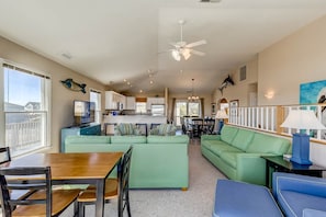 A spacious living area with a green sofa set, a dining table, and a kitchen in the background.