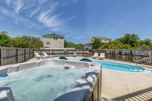 Un jardin avec un jacuzzi et une piscine, entouré de clôtures en bois et de chaises longues.