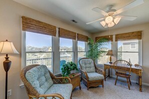 A sunroom with wicker furniture, large windows, and a ceiling fan.