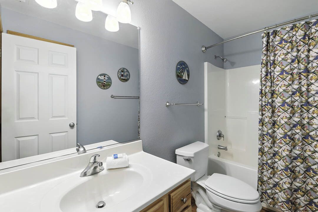A bathroom with a white sink, toilet, and shower. There are wall-mounted towel racks and a door with a simple design.