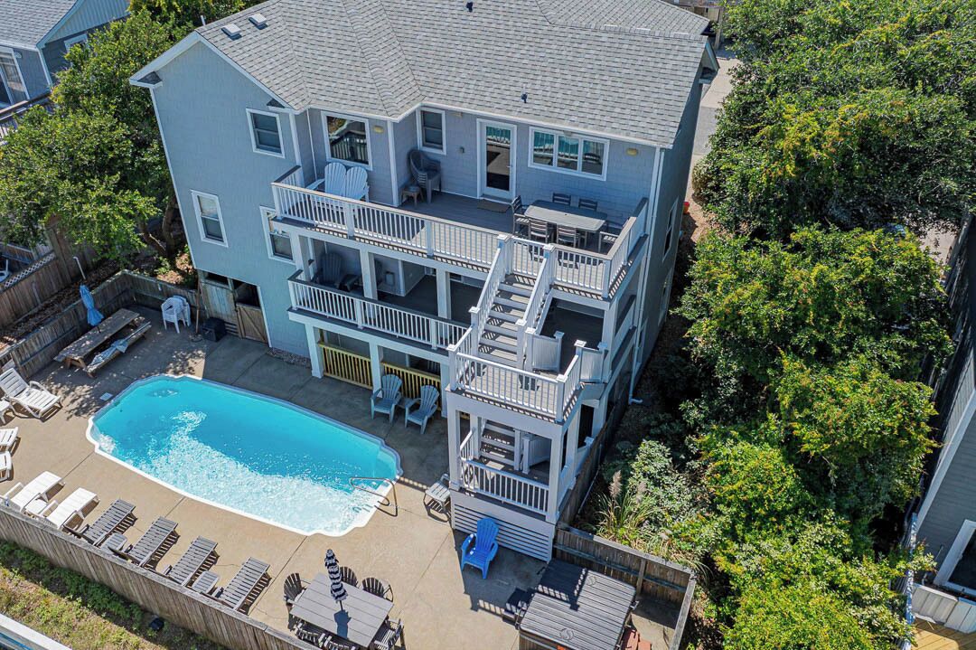 A two-story house with a swimming pool, outdoor seating, and a fenced deck area.