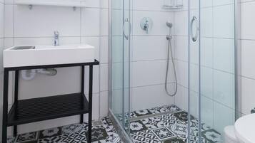 Un baño con ducha separada por mampara de vidrio, lavamanos blanco y baldosas de suelo con estampado.