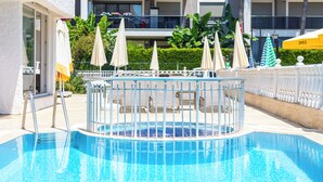 Una piscina con cubierta de metal y sillas de descanso, rodeada de sombrillas y una valla blanca.