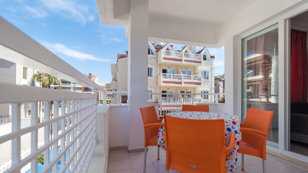 Un balcón con una mesa y sillas, baranda blanca y vistas a edificios cercanos.
