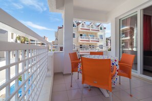 Un balcón con una mesa y sillas, baranda blanca y vistas a edificios cercanos.
