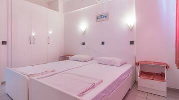 A bedroom with a double bed, a nightstand, a wardrobe, and a small shelf unit.