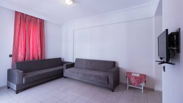 Una sala de estar moderna con dos sofás grises, una cortina roja, una mesita con mantel rojo y un televisor montado.