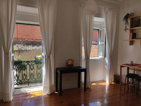 Relax in this serene room with a balcony offering a view, a small table, and a shelf with books and a plant.