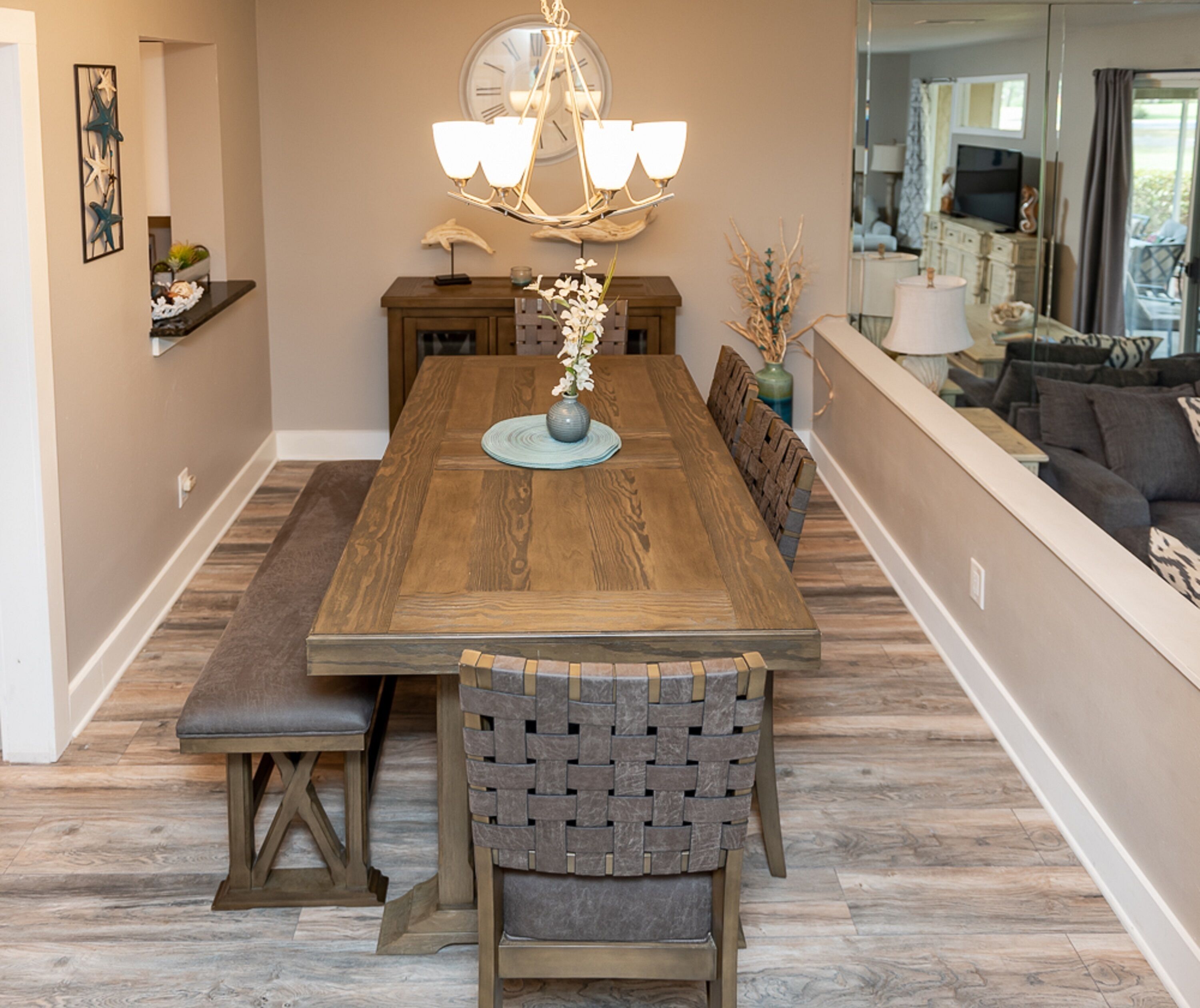 A dining area with a wooden table, bench seating, a chandelier, and a vase with flowers.