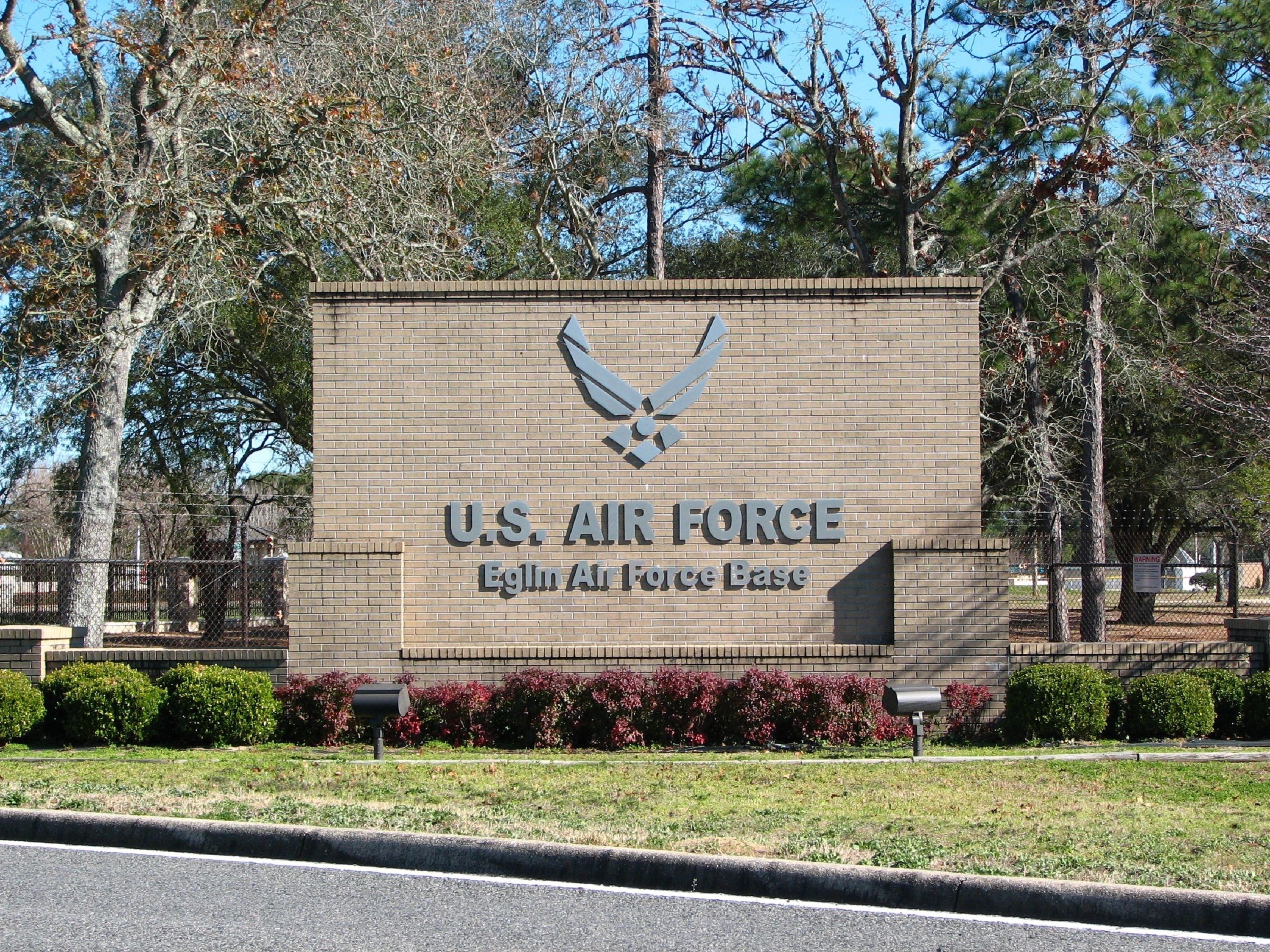 En skylt vid en flygbas tillhörande det amerikanska flygvapnet, med en mur av tegelstenar, en örn som emblem och texten "U.S. AIR FORCE Eglin Air Force Base".
