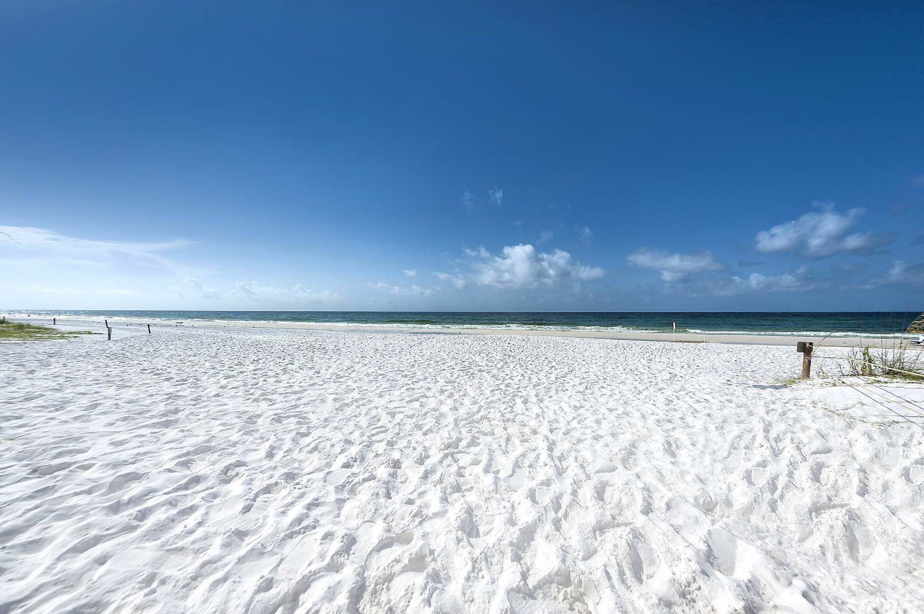 Ein weiter Sandstrand mit blauem Himmel und dem Meer im Hintergrund.