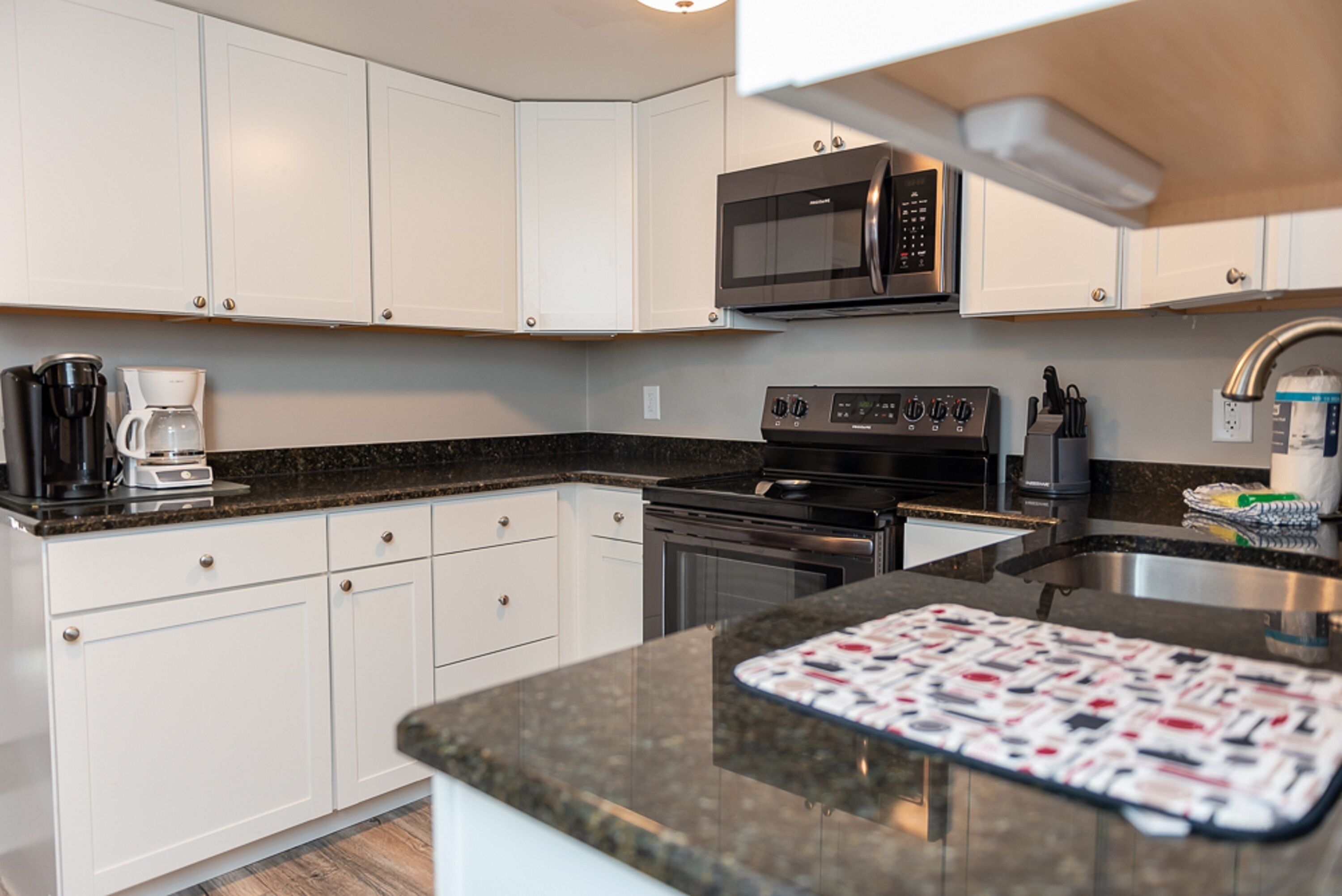 A modern kitchen with white cabinets, a microwave, a coffee maker, and a patterned cutting board.