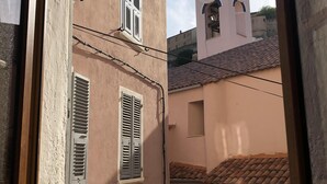A view through a window of a building with a clock tower, featuring a small courtyard with a tiled roof and a door. - Studio in historic district of Corte (Corte)
