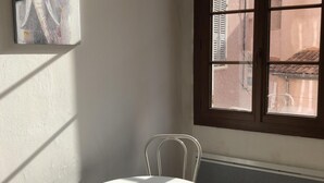 A room with a white table and chairs, a window with a view of buildings, and a radiator under the window. - Studio in historic district of Corte (Corte)