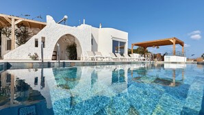 Un espace piscine moderne avec une eau cristalline, des chaises longues et un bâtiment blanc doté d’une architecture originale.