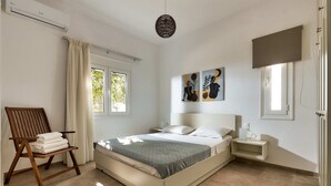 Une chambre à coucher avec un lit, une chaise sur laquelle sont posées des serviettes, une table de chevet et des œuvres d’art accrochées au mur.