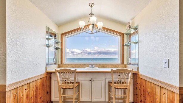 A kitchen with a large window, wooden cabinets, two wicker chairs, and a chandelier. - Sea Spray | 80 ft from the beach | Dog Friendly, Private Pool, Hot Tub | Kitty Hawk (Kitty Hawk)