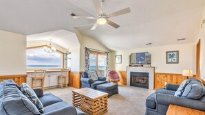 A spacious living area with a ceiling fan, a fireplace, and a view of the ocean. - Sea Spray | 80 ft from the beach | Dog Friendly, Private Pool, Hot Tub | Kitty Hawk (Kitty Hawk)