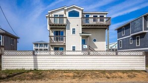A multi-story building with balconies, a white fence, and a sandy ground. - Sea Spray | 80 ft from the beach | Dog Friendly, Private Pool, Hot Tub | Kitty Hawk (Kitty Hawk)