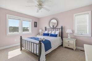 A bedroom with a bed, a nightstand, a dresser, a ceiling fan, and a large window.