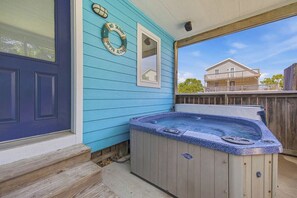 A hot tub on a porch with a blue door and a wooden fence.