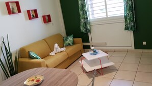A living room with a sofa, a small table, and a window with curtains. - Studio any comfort. (Bas de la Rivière)