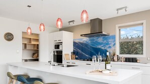 Une cuisine moderne dotée d’un grand îlot central, de tabourets de bar, de luminaires suspendus et offrant une vue sur l’extérieur.