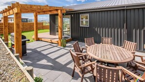 Une terrasse dotée d’une pergola en bois, d’une table ronde entourée de chaises et d’un barbecue.
