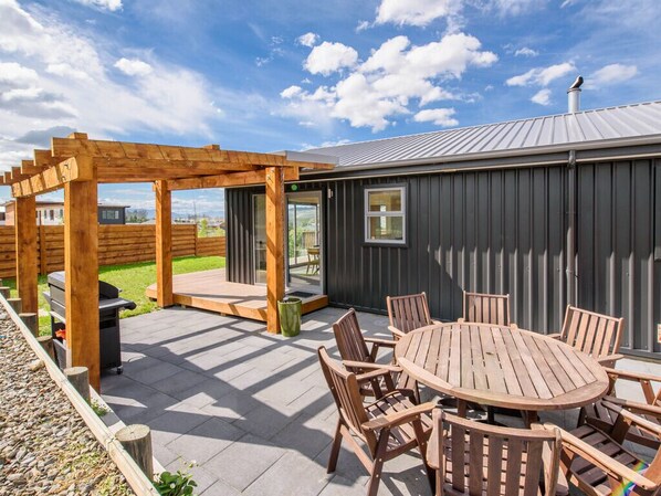 Une terrasse dotée d’une pergola en bois, d’une table ronde entourée de chaises et d’un barbecue.