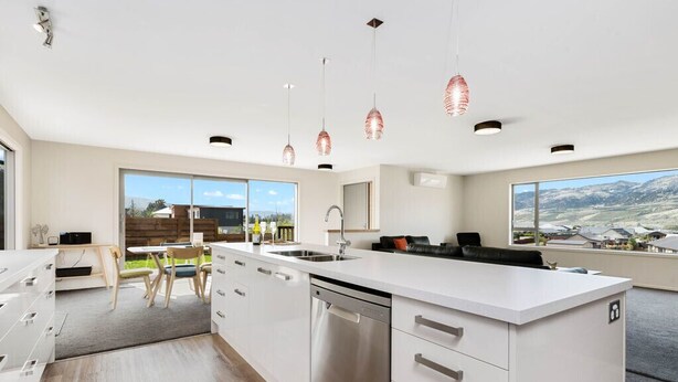 Une cuisine moderne dotée d’un grand îlot central, d’appareils électroménagers en acier inoxydable et de luminaires suspendus.