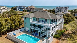 Une grande maison à deux étages dotée d’une piscine, de plusieurs balcons et offrant une vue sur l’océan.