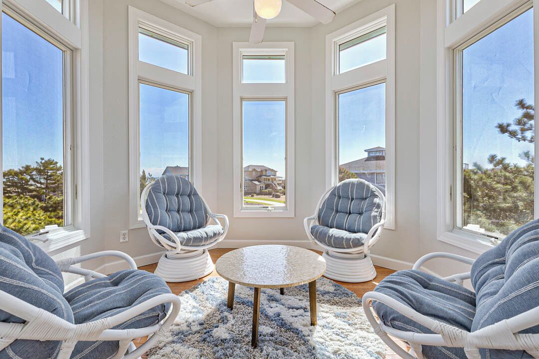 Una habitación con ventanas amplias, dos sillones tapizados, una mesa redonda y una alfombra mullida.