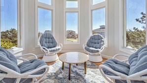 Une pièce dotée de grandes fenêtres, de deux fauteuils rembourrés, d’une table ronde et d’un tapis moelleux.