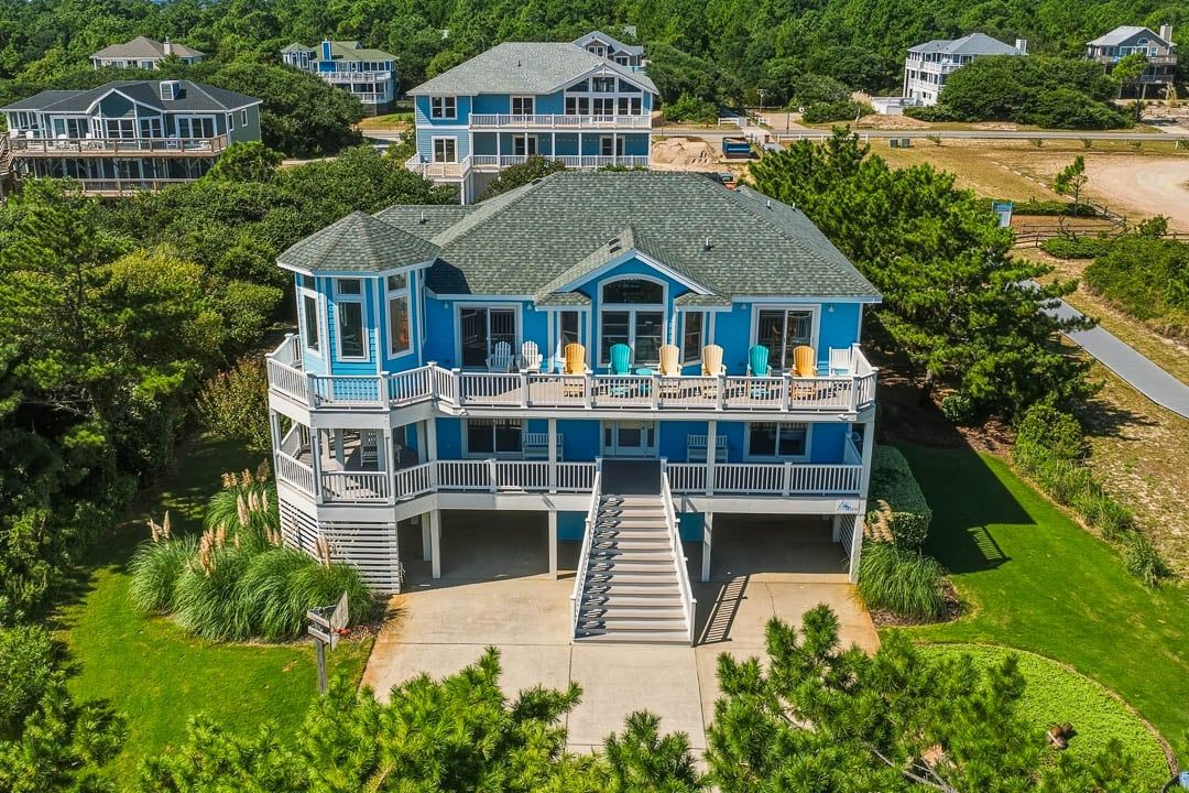 A large blue house with a balcony, surrounded by greenery.