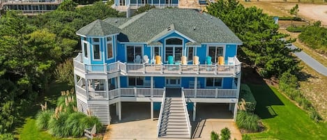 Een groot blauw huis met een balkon, omringd door groen.