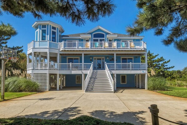 A two-story building with a balcony on the upper level, a staircase leading to the entrance, and a clear sky in the background.