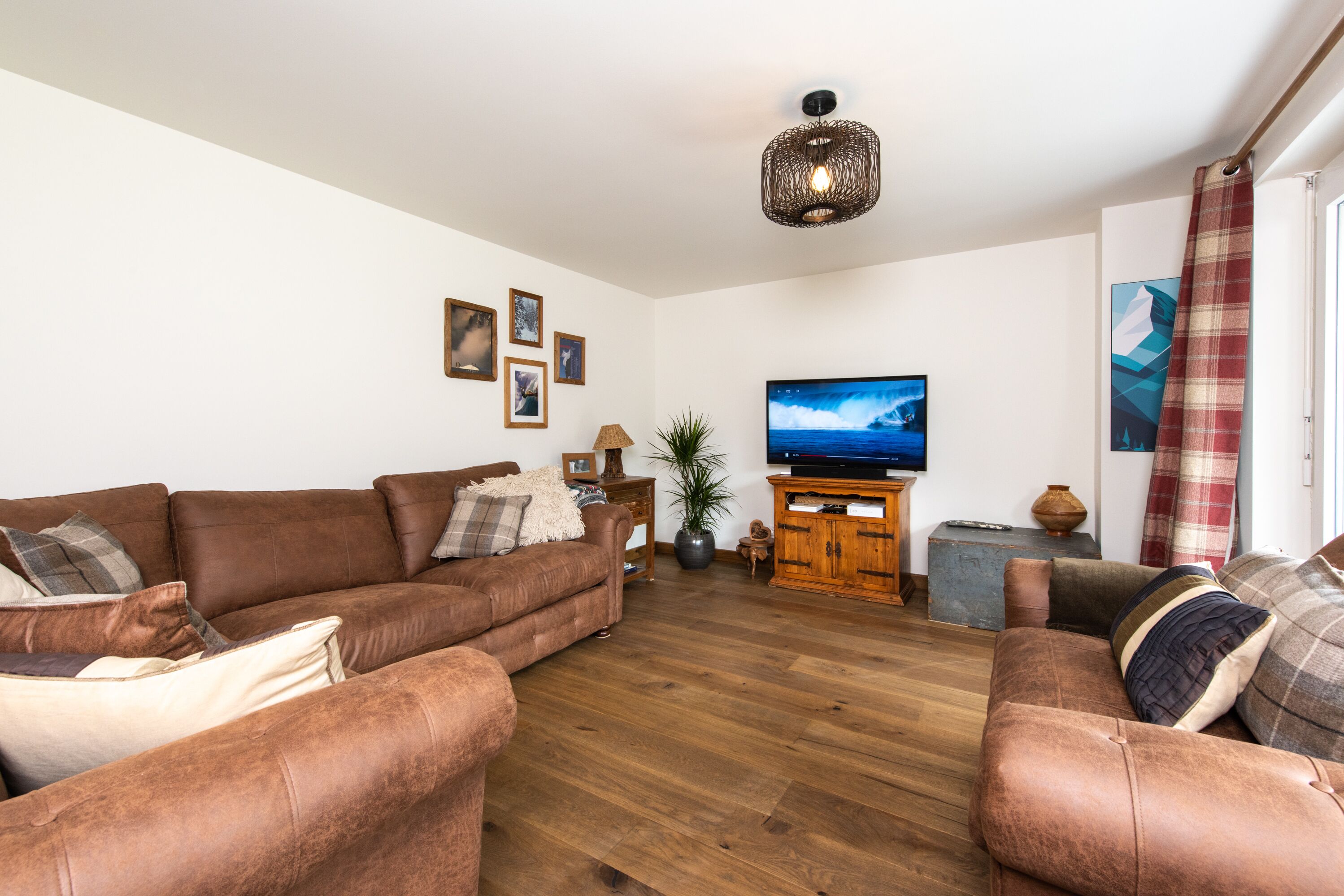 Uma sala de estar com um sofá de couro marrom, um armário de madeira, uma televisão e uma grande janela com vista para o exterior.