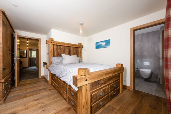 A wooden bed with drawers, a bathroom with a toilet, and a hallway leading to another room.